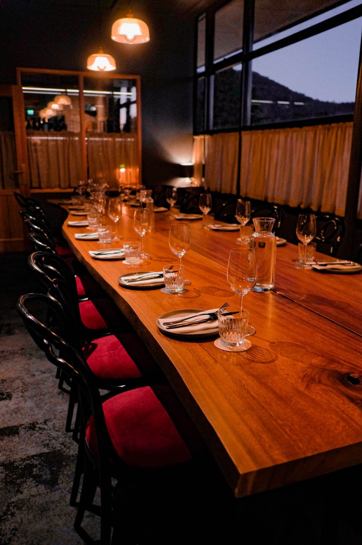 The private dining room: one long timber table set for a party, dusk in the windows