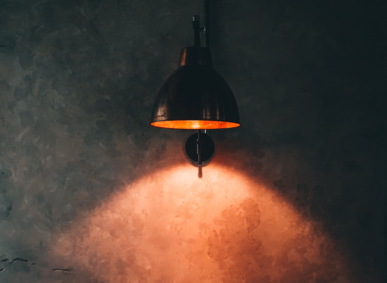 A copper lamp glowing against The Inn's raw concrete wall