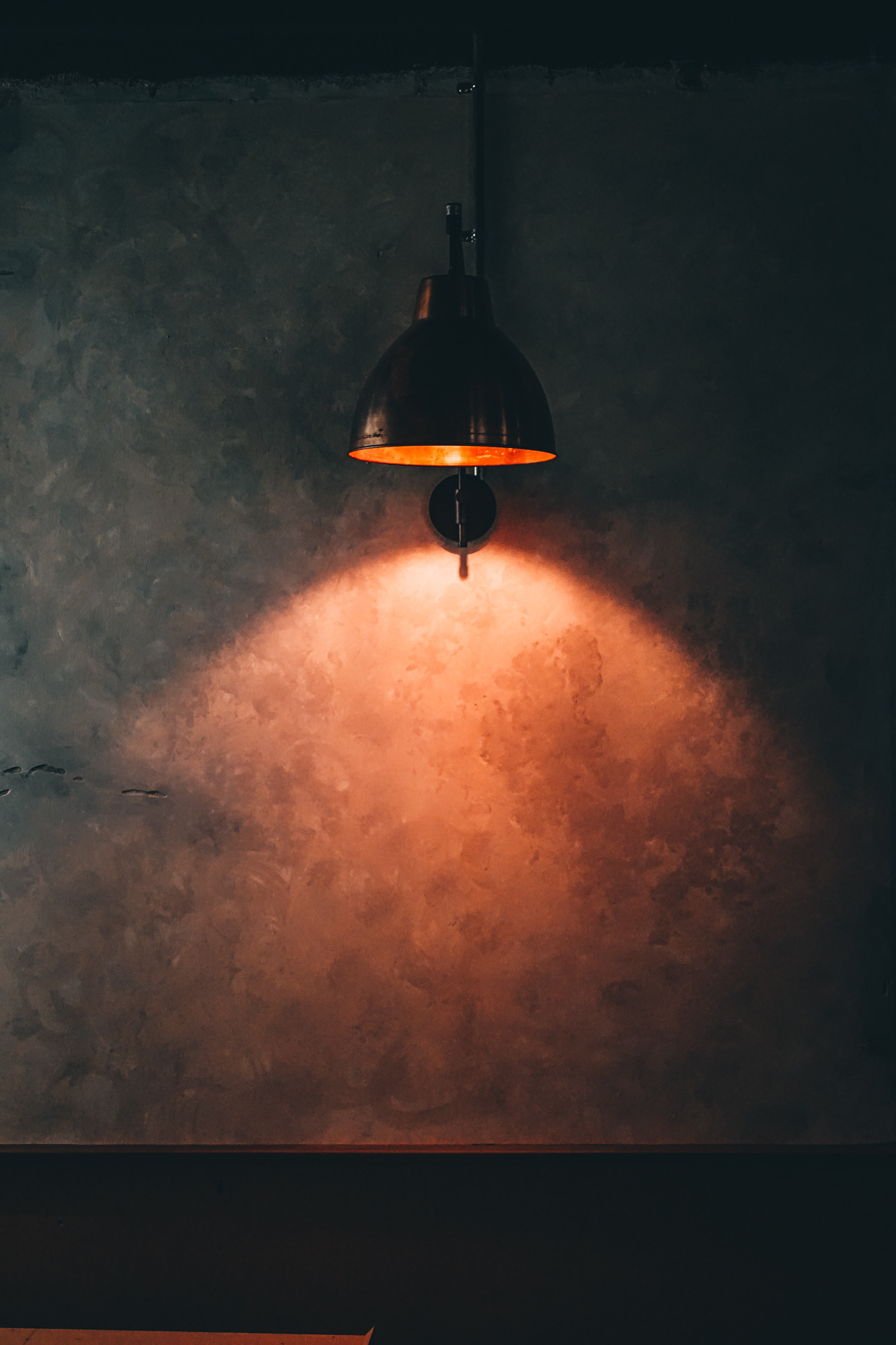 A copper lamp glowing against The Inn's raw concrete wall